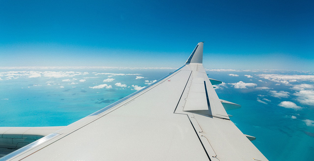 Airfare inflationary spike aircraft wing seen from cabin over clouds