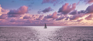 Where in the World 657 featured image Single sailing boat at sea with pink clouds of sunset