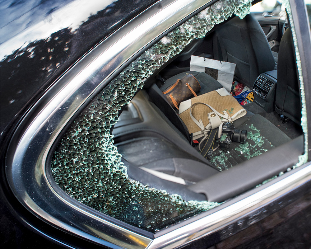 Theft from Rental Cars A smashed side window of a car broken during a robbery. Showing hand bags and a camera on the back seat about to be stolen.